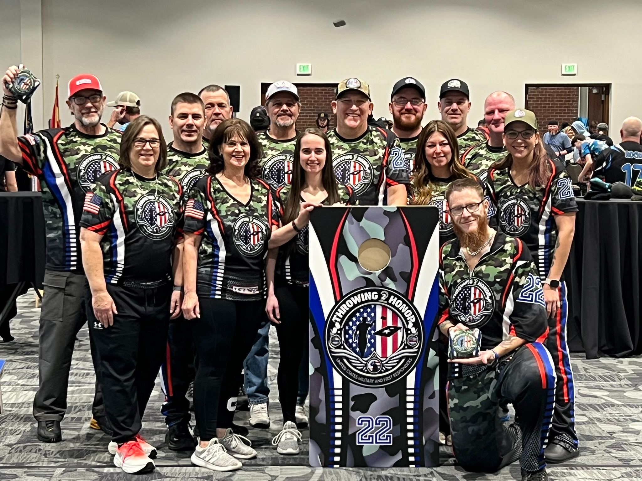 Throwing 2 Honor team photo featuring members in camo jerseys standing around a branded cornhole board